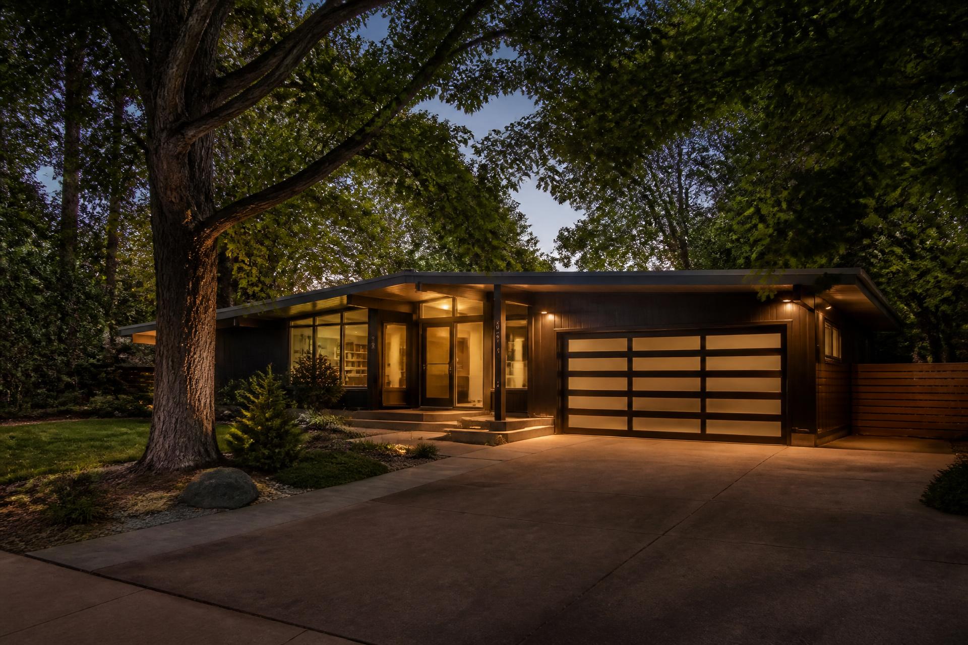 Renovated mid century modern home in Millcreek, Utah glowing at dusk beneath a mature tree canopy