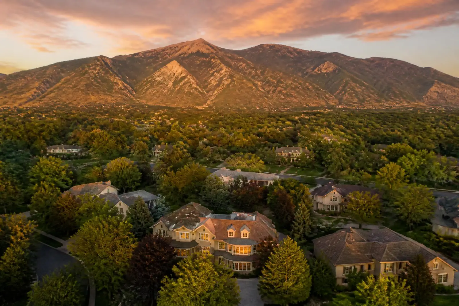 Aerial view of luxury homes under a mature tree canopy in Holladay, Utah with Mount Olympus glowing at sunset